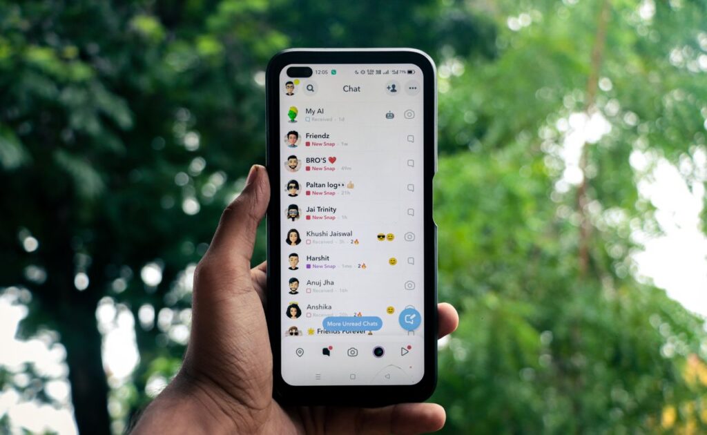 A hand holding a smartphone displaying a chat application outdoors against a green background.